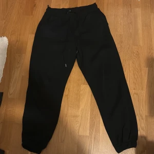 Svarta mjukisbyxor med snörning - Svarta mjukisbyxor med resår i midjan och benslut samt snörning framtill. Perfekta för chill dagar eller när du vill ha det extra bekvämt. Klassisk passform och mjukt material.