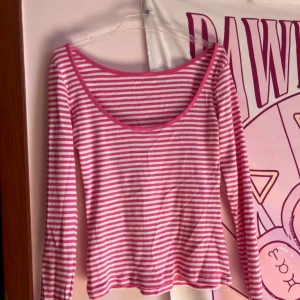 Rosa och vit randig långärmad topp - Säljer en långärmad topp från Rainbow i rosa och vitt med smala ränder. Toppen har en rundad, lite djupare halsringning och är i mjuk, stretchig bomull. Perfekt för dig som gillar färg och vill ha en enkel men söt bas i garderoben.
