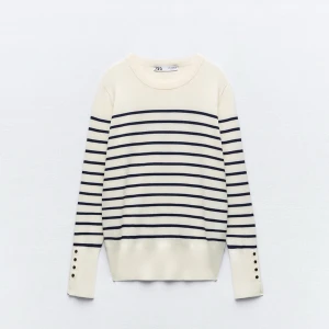 Randig vit och marinblå tröja från Zara - Snygg vit tröja med marinblå ränder från Zara. Tröjan har långärmade ärmar med dekorativa knappar vid mudden och en rund halsringning. Endast använd ett fåtal gånger, som ny.