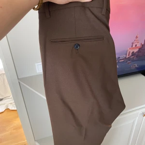 Bruna kostymbyxor med rak passform - Snygga bruna kostymbyxor med klassisk rak passform och pressveck. Storlen 32/31