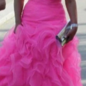 Rosa långklänning med volanger - Säljer en superfin långklänning i stark rosa med axelbandslös design och hjärtformad urringning. Överdelen har glittriga detaljer och kjolen är täckt av stora volanger i flera lager. Perfekt för bal eller liknande tillfällen. Nypris 5000, använd en gång och kvitto finns