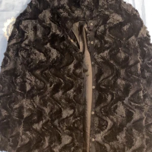 Svart pälsjacka från Vero Moda - Säljer en svart pälsjacka från Vero Moda med snyggt vågigt mönster i pälsen. Jackan har knappar framtill och är fodrad med glansigt tyg. Perfekt för dig som vill sticka ut med en trendig och mysig look. Står att de är storlek S men den är mycket större än vad den ser ut att vara så jag skulle rekommendera till någon som har storlek M 