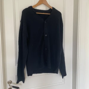 Svart kofta från 157, storlek M - Mysig svart kofta från 157 i storlek M. Koftan har en enkel design med knappar framtill och lång ärm. Perfekt att slänga på sig över en t-shirt eller linne. Materialet känns stickat och ger en avslappnad vibe.