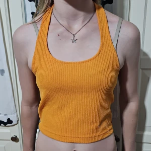 Ribbad orange linnetopp från Divided - Säljer en ribbad orange linnetopp från Divided. Toppen är croppad med breda axelband och öppen rygg, perfekt för varma dagar. Materialet är mjukt och stretchigt, vilket gör den riktigt bekväm. Snygg att styla med jeans eller kjol för en cool look.