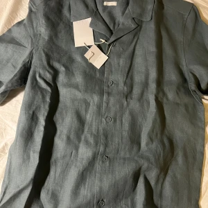 Grå linneskjorta med knappar - Snygg grå skjorta från Zara i 100% linne. Skjortan har klassisk krage, korta ärmar och knäppning framtill. Perfekt för en chill och stilren look. Enkel och luftig design som passar till många outfits.