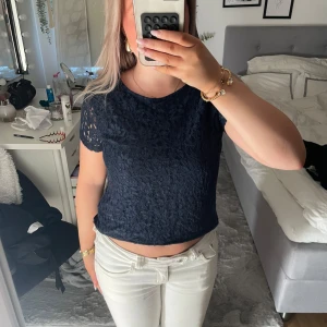 Mörkblå blommig spetsblus S - Säljer en mörkblå blus i storlek S med blommigt spetsmönster framtill och på ärmarna. Toppen har rund halsringning och korta ärmar, med en mjuk baksida i bomull. Perfekt för dig som gillar romantiska detaljer och en feminin look.