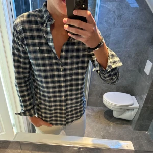 Rutig skjorta från Ralph Lauren - Snygg rutig skjorta från Ralph Lauren i blått och vitt. Klassisk button-down krage, långärmad och med broderad logga på bröstet. Skjortan är i mjuk bomull och har en normal passform med knappar framtill. Jag är 188cm på bilden. Pris kan diskuteras! Hör av er vid frågor;)