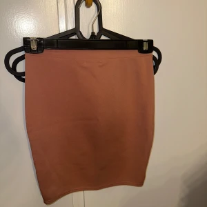 Nuderosa tight kjol från NLY One XS - Enkel och stilren nuderosa kjol från NLY One i tight passform. Kjolen är kort och har en rak, figurnära siluett utan detaljer eller mönster. Tillverkad i mjukt och stretchigt material som sitter snyggt på kroppen.