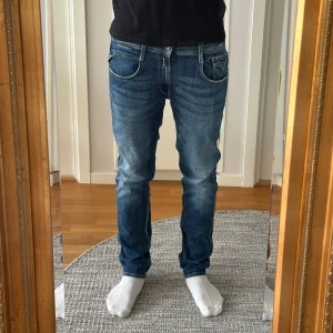 Blå Replay Anbass jeans slim fit - Säljer ett par blå Replay Anbass jeans med snygg tvätt och klassiska detaljer. Jeansen har fem fickor, läderpatch bak och smal passform. De är tillverkade i stretchig denim för extra komfort och har en modern look med lätt slitning på låren.