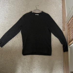 Mörkgrå stickad tröja från Zara - Mysig mörkgrå stickad tröja från Zara med rund halsringning och ribbade muddar. Perfekt för kyliga dagar och enkel att matcha med jeans eller kjol. Klassisk modell med lång ärm och mjukt material. OBS: krympt till S