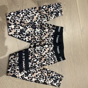 Leopardmönstrade leggings från Stronger - Snygga leopardmönstrade leggings från Stronger med svart resår i midjan där loggan syns tydligt. De har en tight passform och är perfekta för träning. Materialet är stretchigt och bekvämt, vilket gör dem grymma för aktiva dagar. Bara använda en eller två gånger.