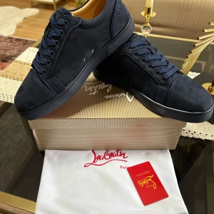 Mörkblå sneakers från Christian Louboutin - Snygga mörkblå sneakers från Christian Louboutin i mocka med ton-i-ton broderad logga på hälen. Skorna har rund tå, platt sula och klassisk snörning. Insidan är fodrad i beige läder för extra komfort. Perfekta för dig som vill ha en stilren och lyxig look.
