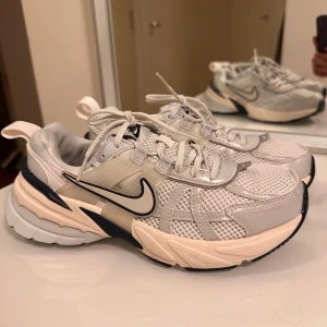 Nike sneakers i vitt och beige mesh - Nike sneakers med chunky sula i vitt, beige och mörkblått. Ovandel i mesh och syntet med snygga detaljer och svart swoosh på sidan. Skorna har snörning och platt sula, perfekt för en sportig och trendig look.