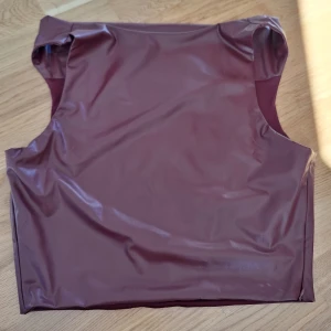 Vinröd ärmlös topp i skinnimitation S/M - Säljer en vinröd ärmlös topp i skinnimitation med slät yta och rund halsringning. Toppen har en croppad passform och är fodrad på insidan för extra komfort. Perfekt för dig som vill sticka ut med en edgy look. Helt nytt, tyvärr inga lappar kvar. 