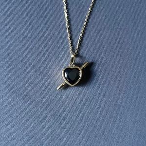 Rebel Heart – Golden Noir - Guldpläterat halsband i rost- och nickelfritt stål. Svart hjärta med pil. Kedja 50 cm, justerbar. Hängets diameter 0,9 cm. 