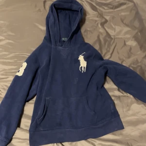 Mörkblå big pony  hoodie från Polo Ralph Lauren  - Mörkblå hoodie från Polo Ralph Lauren med stor vit logga på bröstet och siffra 3 på ena ärmen. Klassisk känguruficka framtill och huva. Perfekt för en chill och sportig look.