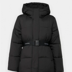 Svart pufferjacka från Calvin Klein - Snygg svart pufferjacka från Calvin Klein med huva och markerat midjebälte med logga. Jackan har en quiltad look, dragkedja framtill och är perfekt för kalla dagar. Oversized passform och långa ärmar ger en cool och modern vibe. Pris går att diskutera!‼️