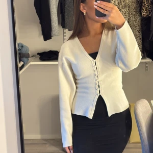Vit v-ringad blus med knappar - Snygg vit blus med v-ringning och dekorativa knappar framtill. Modellen är figurnära upptill och har långa ärmar. Perfekt att styla med kjol eller jeans för en clean look.