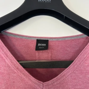 Rosa v-ringad tröja från Hugo Boss - Snygg rosa v-ringad tröja från Hugo Boss i slim fit-modell. Tröjan har långa ärmar och ribbade muddar vid nederkant och ärmslut. Sparsamt använd, storlek L