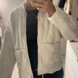 Quiltad beige jacka från Zara - Säljer en quiltad beige jacka från Zara i storlek S. Jackan har en boxig passform, dragkedja framtill och två stora fickor. Materialet känns mjukt och jackan har ett vågigt quiltmönster som ger en chill vibe. Perfekt att slänga på sig över en hoodie eller t-shirt. Ända defekten är på sista bilden.