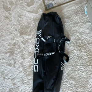 Svart sportväska från Oxdog - Stor svart sportväska från Oxdog med vit logga och text på både väskan och handtagen. Väskan är avlång och har dragkedja längs ovansidan, perfekt för att bära sportutrustning. Tillverkad i slitstark syntet med praktiska bärhandtag.