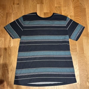 Randig t-shirt från We Style, marinblå - Snygg marinblå t-shirt från We Style i storlek L med smal passform. T-shirten har breda och smala ränder i blått och vitt, rund halsringning och är tillverkad i mjuk bomull. Perfekt för en avslappnad och stilren look.