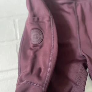 Vinröda ridleggings från Kingsland - Säljer ett par vinröda ridleggings från Kingsland med hög midja och tight passform. Byxorna har silikonmönster på insidan av benen för extra grepp och diskret logga på benet. Perfekta för ridning och tillverkade i stretchigt syntetmaterial. Knappt använda. Nypris: ca 1200 