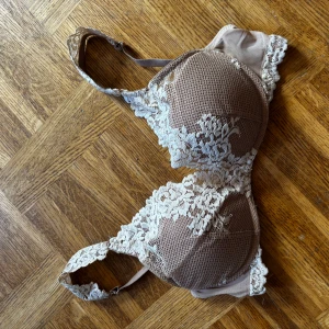 Beige spets-bh från Intimissimi - Säljer en snygg beige bh från Intimissimi med vacker vit spetsdetalj över kuporna och axelbanden. Bh:n har en feminin design med blommönstrad spets och justerbara axelband. Perfekt för dig som gillar en romantisk och elegant look.