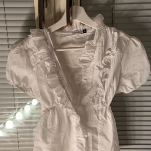 Vit omlott topp med volang - ‼️‼️PRIS KAN SÄNKAS‼️‼️Supersöt vit omlott topp från Sedi Paris med puffärmar och volangdetaljer längs v-ringningen. Klänningen har knappar framtill och är perfekt för en fräsch och romantisk look. Tillverkad i lätt bomull som känns luftig och skön. Använts 2-3 gånger 