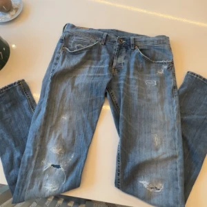 Dondup jeans - Säljer ett par blå dondup jeans från George i storlek 33 skinny fit. Jeansen har slitna detaljer och hål på framsidan för en cool, avslappnad look. Klassisk femficksmodell med ljus tvätt och synliga sömmar. Perfekt för dig som gillar grish