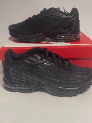 Nike TN 3 svarta sneakers - Svarta Nike tn 3 sneakers med chunky sula och synliga luftkuddar. Ovandelen är i en mix av syntet och mesh med snygga detaljer och snörning. Skon har en sportig vibe och passar perfekt för dig som gillar streetwear och vill ha en clean look.
