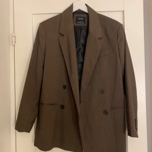 Brun oversized kavaj från Bershka - Snygg brun kavaj från Bershka i storlek XS. Dubbelknäppt med svarta knappar, klassisk krage och fickor fram. Lätt oversized passform och helfodrad insida. Perfekt för dig som gillar stilrena och tidlösa plagg. Aldrig använd.