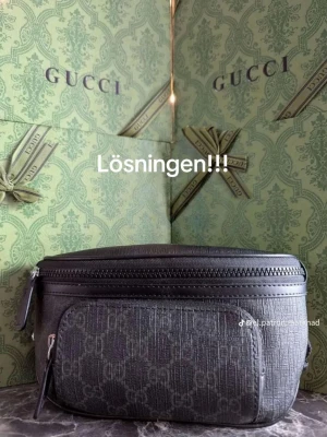 Svart Gucci axelväska med monogram - Säljer en svart axelväska från Gucci med diskret GG-monogram över hela väskan. Väskan har en praktisk dragkedja upptill och ett extra fack framtill. Justerbart band med spänne gör den enkel att bära crossbody eller runt midjan. Materialet är präglat skinn med lyxig känsla. Box medföljer ej 