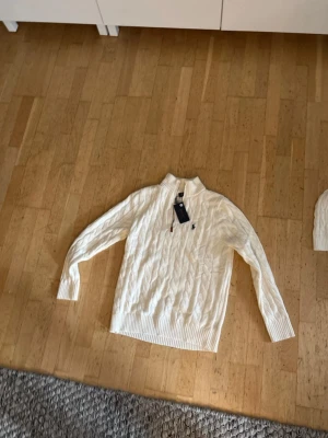 Vit stickad half zip-tröja Polo Ralph Lauren - Säljer en vit stickad tröja från Polo Ralph Lauren i storlek L. Tröjan har ett snyggt kabelstickat mönster, half zip-dragkedja och ribbad krage. Klassisk logga broderad på bröstet. Perfekt för dig som gillar stilrena och tidlösa plagg.