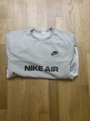 Grå sweatshirt Nike Air - Säljer en grå sweatshirt från Nike Air med stora logotryck både fram och bak. Tröjan har rund hals, långa ärmar och kontrastpaneler i ljusgrått. Perfekt för dig som gillar sportig och avslappnad stil. Materialet är mjuk bomullsmix som känns skön mot huden.