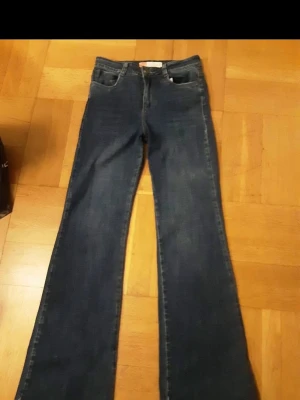 Blå bootcut jeans - Säljer ett par snygga blå jeans med bootcut-snitt. Klassisk femficksmodell med dragkedja och knapp framtill. Jeansen har en mörkblå tvätt och är tillverkade i jeansmaterial som ger en cool och tidlös look.