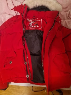Röd dunjacka Moose Knuckles - Säljer en röd dunjacka från Moose Knuckles med fet päls på luvan och ikoniska metallringar på ärmen. Söker byten för en svart moose jacka eller canada goose