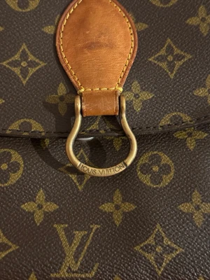 Louis Vuitton brun axelväska monogram - Säljer en klassisk brun axelväska från Louis Vuitton med ikoniskt monogrammönster i beige och guld. Väskan har justerbar rem i skinn, guldfärgad metallring och detaljer i läder. Perfekt storlek för det viktigaste och riktigt snygg att bära crossbody.