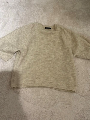 Beige stickad tröja från Gina Tricot - Mysig beige stickad tröja från Gina Tricot i storlek XS. Tröjan har rund hals och långa ärmar med ribbade muddar. Perfekt för lager-på-lager och chill dagar. Enkel och stilren design som funkar till många olika outfits.