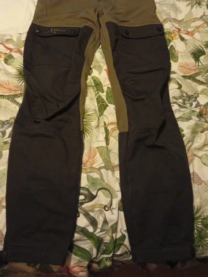 High Mountain cargopants - Säljer ett par cargopants från High Mountain i storlek 160. Byxorna är tvåfärgade med gröna och svarta paneler, har flera fickor med knappar och dragkedja, samt robusta detaljer. Perfekta för dig som gillar outdoor och äventyr.