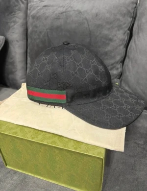 Svart Gucci keps med GG-mönster (Äkta) - Snygg svart keps från Gucci med klassiskt GG-monogram över hela kepsen och ikoniska gröna och röda ränder på sidan. Kepsen har böjd skärm och är tillverkad i slitstark polyester. Perfekt för dig som vill ha en lyxig streetstyle-accessoar.