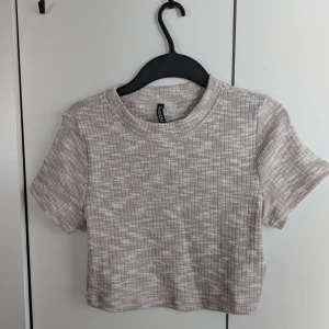 Beige ribbad croppad topp från Divided - Säljer en beige ribbad croppad topp från Divided. Den har korta ärmar och ett diskret mönster som ger en stilren look. Perfekt för en avslappnad stil. Hör av dig vid intresse!