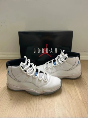 Nike Air Jordan 11 vit/blå sneakers - Nike Air Jordan 11 sneakers i vit och ljusblå färg med högt skaft och rund tå. Skorna har snörning, platt sula och ikonisk Jumpman-logga på sidan. Materialet är en mix av skinn och syntet, med svart insida och detaljer i blått. Perfekt för dig som gillar klassiska basketmodeller. All stains are removable with soap