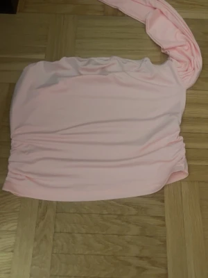 Ljusrosa oneshoulder tubtopp i polyester - Säljer en ljusrosa tubtopp med oneshoulder-design i storlek L. Toppen är tillverkad av mjuk och stretchig polyester med elastan, vilket gör den bekväm och följsam. Perfekt för dig som gillar en enkel men snygg look med lite extra edge.