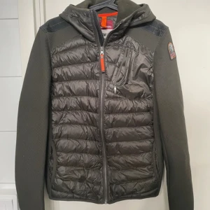 Mörkgrön dunjacka Parajumpers S - Snygg mörkgrön dunjacka från Parajumpers med huva och orange detaljer. Jackan har quiltad framsida och rygg, släta ärmar och dragkedja framtill. Märkespatch på ena ärmen och praktiska fickor med dragkedja. Perfekt för kyliga dagar. Skriv om ni har frågor och kom gärna med bud! Jackan har en liten skada på framsidan längst ner men jag har bara satt en liten bit tejp över den och det syns inte riktigt 