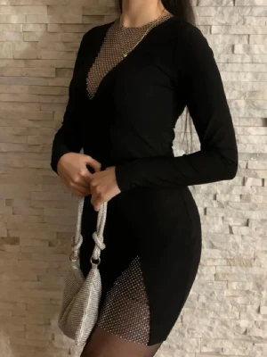 Svart klänning med glittriga detaljer - Snygg svart klänning med långärmade och glittriga meshpartier vid halsringningen och på sidan av kjolen. Klänningen har en tight passform och ger en cool och trendig look med sina glittriga inslag. Perfekt för dig som vill sticka ut med stil.