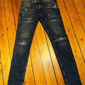 Replay Sustainable Lab 28/32 - Säljer ett par Replay jeans i blå tvätt med slitna detaljer och skinny passform. Klassisk femficksmodell med låg midja och smala ben. Jeansen är tillverkade i stretchig denim för extra komfort och har snygga slitningar framtill och på bakfickorna.
