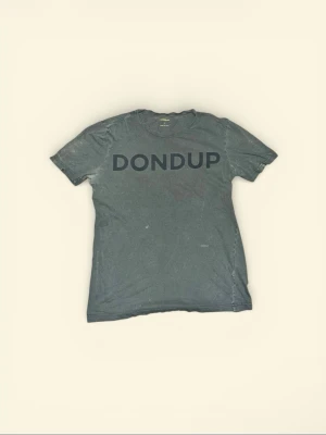Grå t-shirt från Dondup med tryck - Säljer en grå t-shirt från Dondup i storlek L, tillverkad i Italien. T-shirten har ett stort svart Dondup-tryck på bröstet och klassisk rund hals. Modellen är kortärmad och har en enkel, clean look som funkar till jeans eller shorts.