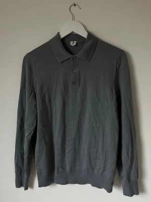 Mörkgrå pikétröja från ARKET - Snygg mörkgrå långärmad pikétröja från ARKET i mjuk bomull. Klassisk krage med tre knappar framtill och ribbade muddar vid ärmslut och nederkant. Perfekt för en clean och stilren look. 6Q10