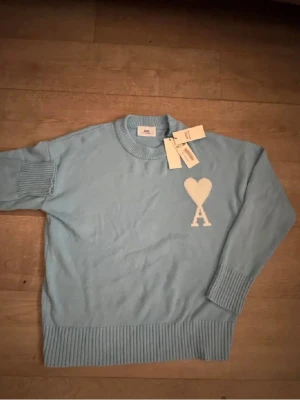 Ljusblå stickad tröja från Ami - Säljer en ljusblå stickad tröja från Ami Alexandre Mattiussi i storlek S. Tröjan har ett vitt hjärta med bokstaven A broderat på bröstet, rund hals och ribbade muddar vid ärmslut och nederkant. Perfekt för dig som gillar stilrena detaljer.